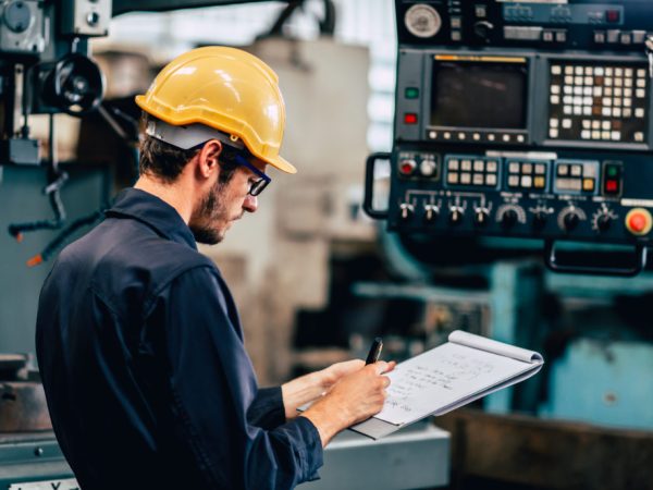 young profession technician engineer operate heavy machine to automated CNC in factory, worker with check list.