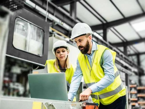 A portrait of an industrial man and woman engineer with laptop in a factory, working.